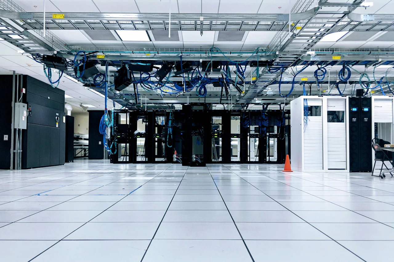 Ruang data center dengan kabinet jaringan, jalur kabel di atas rak, dan raised floor